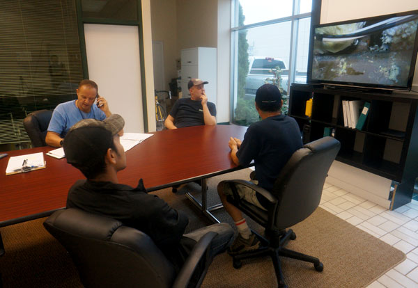 four men in a boardroom looking at a flat screen tv