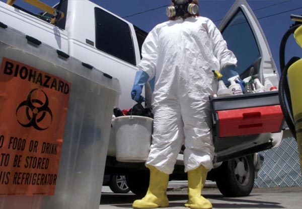 man in hazmat suit carrying chemicals standing in front of a mobile unit vehicle