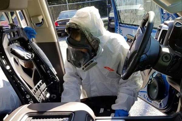 Guy cleaning a car and sanitizing with a hazmat suit on